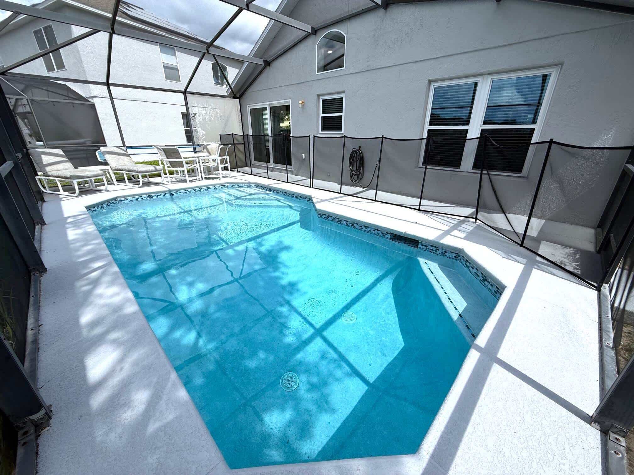 A rectangular swimming pool with a clear blue water, surrounded by a white deck and a metal fence.