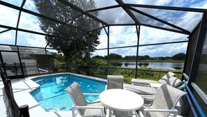 Área externa coberta com piscina, espreguiçadeiras e vista para um lago.
