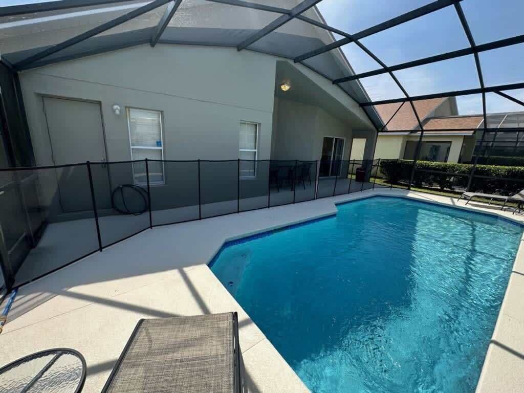 Una piscina interior con techo de vidrio, rodeada por una valla, y un área de descanso con una silla.