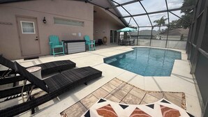 A covered outdoor swimming pool with lounge chairs, a table, and a patio area.