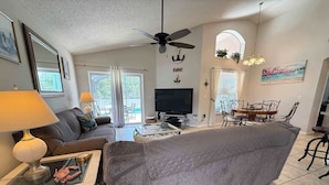 A living room with a sofa, TV, dining table, and ceiling fan.