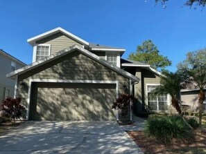 A two-story house with a garage, a sloped roof, and a front yard with landscaping. - Beautiful Remodeled Private Pool Home (Haines City)