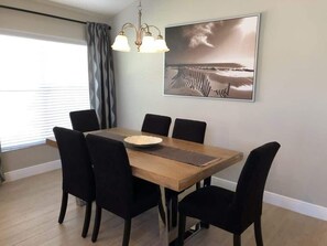 A dining room with a wooden table, six black chairs, a chandelier, and a framed picture on the wall. - Beautiful Remodeled Private Pool Home (Haines City)