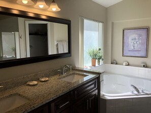 A bathroom with a granite countertop, a double sink, a large mirror, a bathtub, and a window with a plant. - Golf Course Views, Southern Dunes Villa (Haines City)