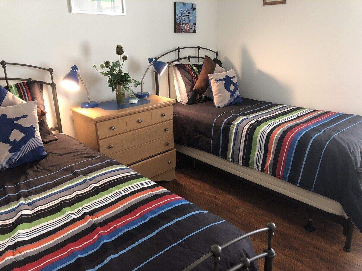 Une chambre avec deux lits, une table de chevet, une commode, une lampe et une œuvre d’art murale.