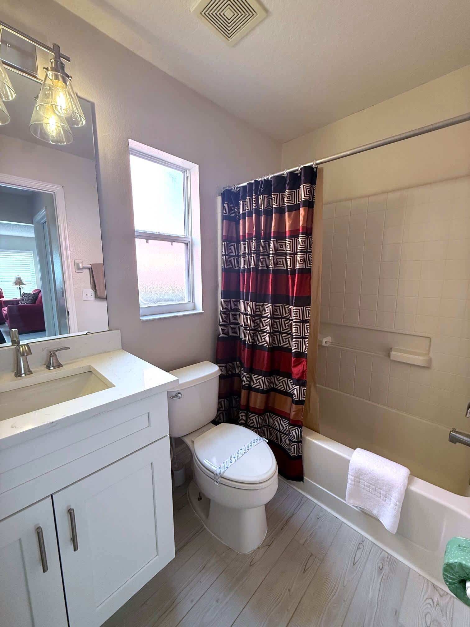 A bathroom with a white toilet, a sink with a mirror, a shower curtain, and a bathtub.