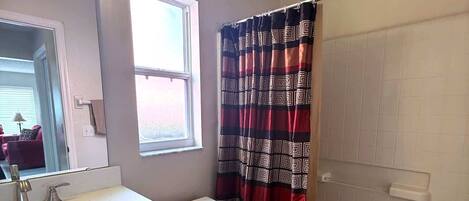 A bathroom with a white toilet, a sink with a mirror, a shower curtain, and a bathtub.