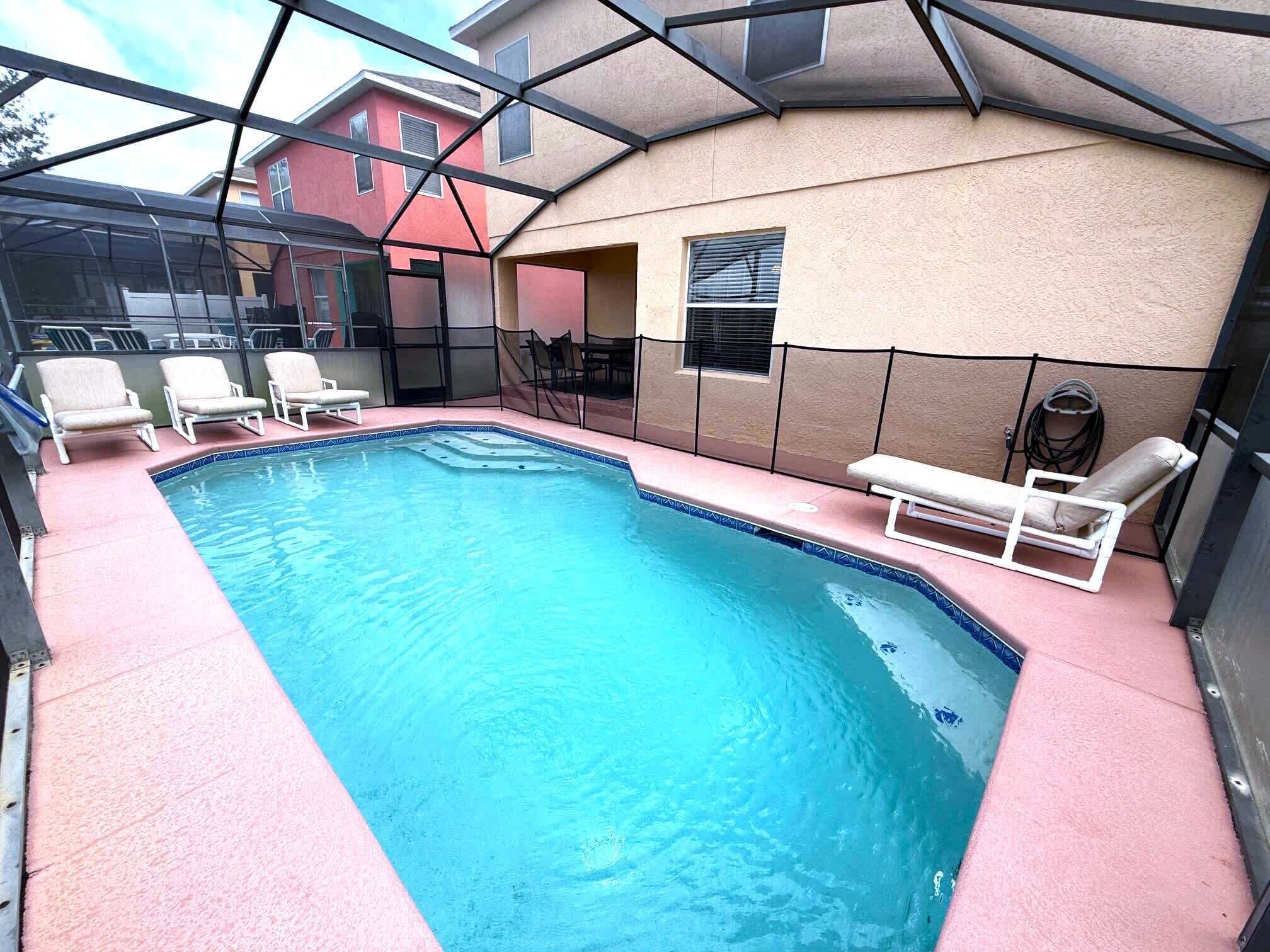 A swimming pool with a glass enclosure, surrounded by lounge chairs and a bench.