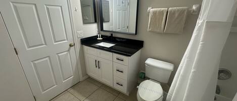 A bathroom with a white toilet, a black sink, a mirror above the sink, and a shower curtain.
