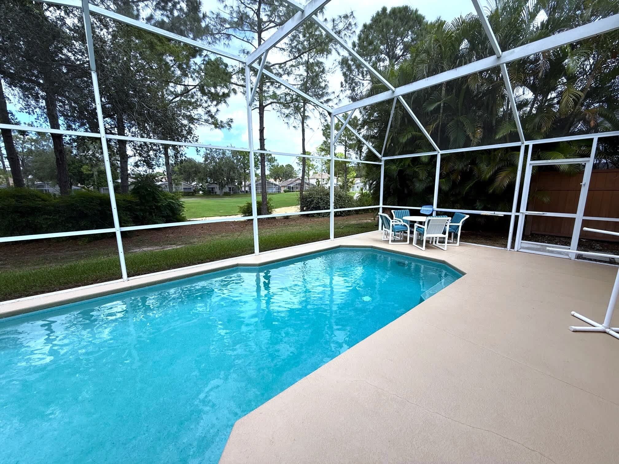 A covered swimming pool with a clear view of the surrounding landscape, including trees and a lawn.