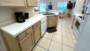 Una cocina con encimera blanca, armarios de madera, lavavajillas, fregadero y estufa.