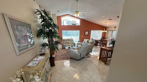 A spacious living room with a large potted plant, a sofa, and a dining area with a table and chairs. - Upgraded Pool Villa, Spa, Southern Dunes (Haines City)