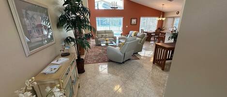 A spacious living room with a large potted plant, a sofa, and a dining area with a table and chairs.