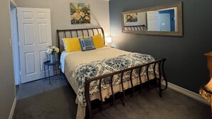 Un dormitorio con cama, ventilador de techo, un cuadro, un espejo y una puerta.