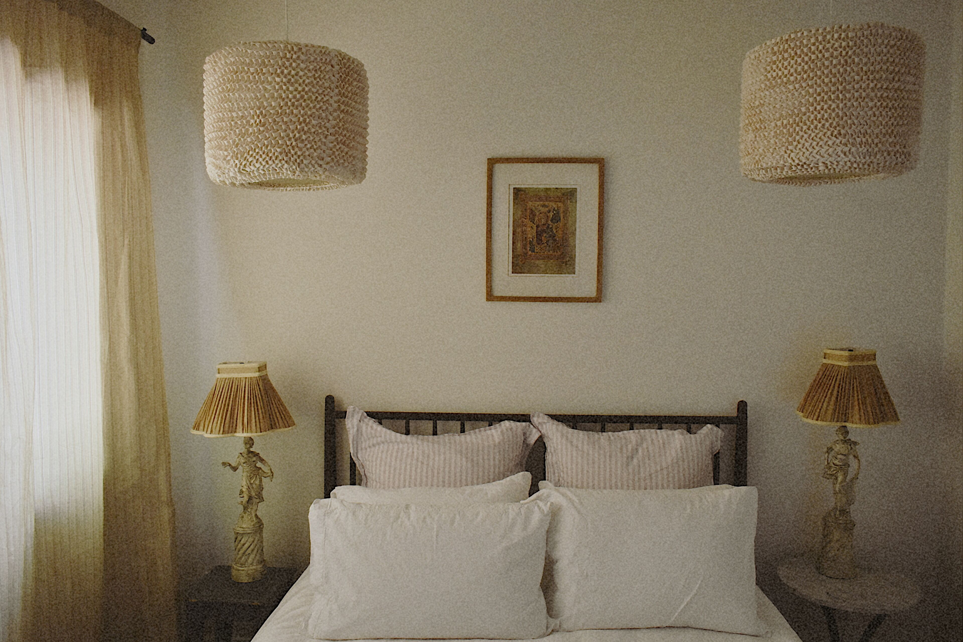 A bedroom with a bed, two bedside lamps, a framed picture on the wall, and a window with curtains.