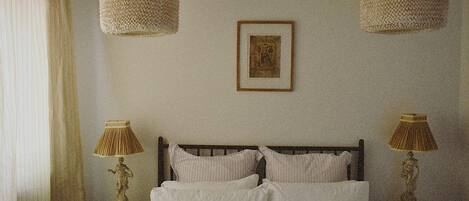 A bedroom with a bed, two bedside lamps, a framed picture on the wall, and a window with curtains.