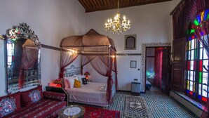 A traditional room with a four-poster bed, a red sofa, a chandelier, and a colorful stained glass window. - Riad Lalla Zoubida (Fes)