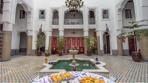 A courtyard with a fountain, tiled floor, and a table with food. - Riad Lalla Zoubida (Fes)