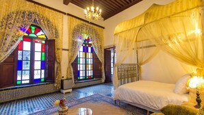 A room with a bed, a chandelier, and a window with stained glass. - Riad Lalla Zoubida (Fes)