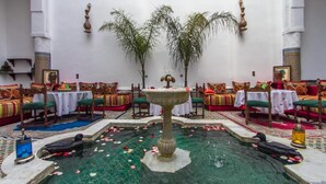 A traditional Moroccan riad with ornate furniture, a central fountain, and a pool surrounded by palm trees. - Riad Lalla Zoubida (Fes)
