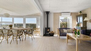 Un vaste salon doté d’un haut plafond, d’une cheminée, d’un coin repas avec des chaises et offrant une vue dégagée grâce à de grandes fenêtres.