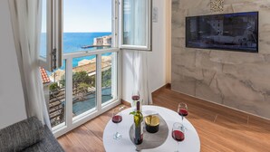 A room with a large window overlooking a coastal view, a round table with wine glasses and a bottle, and a wall-mounted information board. - Charming 2-bedroom apartment with WiFi, AC in lovely Dubrovnik (Dubrovnik)