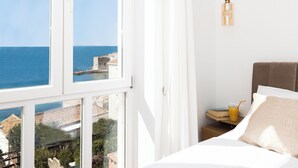 A hotel room with a bed, a nightstand with a drink, and a view of the sea and buildings. - Charming 2-bedroom apartment with WiFi, AC in lovely Dubrovnik (Dubrovnik)