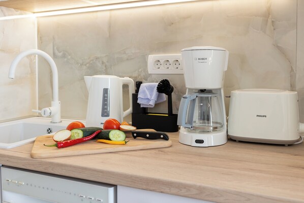 Une cuisine moderne équipée d’un évier, d’une machine à café Bosch, d’un grille-pain Philips et d’une planche à découper avec des légumes.