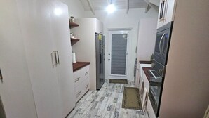 Cocina compacta con armarios blancos, un refrigerador, un horno y un microondas. Cuenta con una zona de comedor con una mesa y una silla.