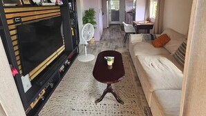 Una sala de estar con un mueble negro para entretenimiento, un sofá blanco, una mesita y un ventilador.