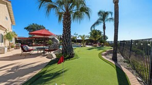 Un área de piscina con campo de práctica de golf, sillas de descanso y una sombrilla roja.
