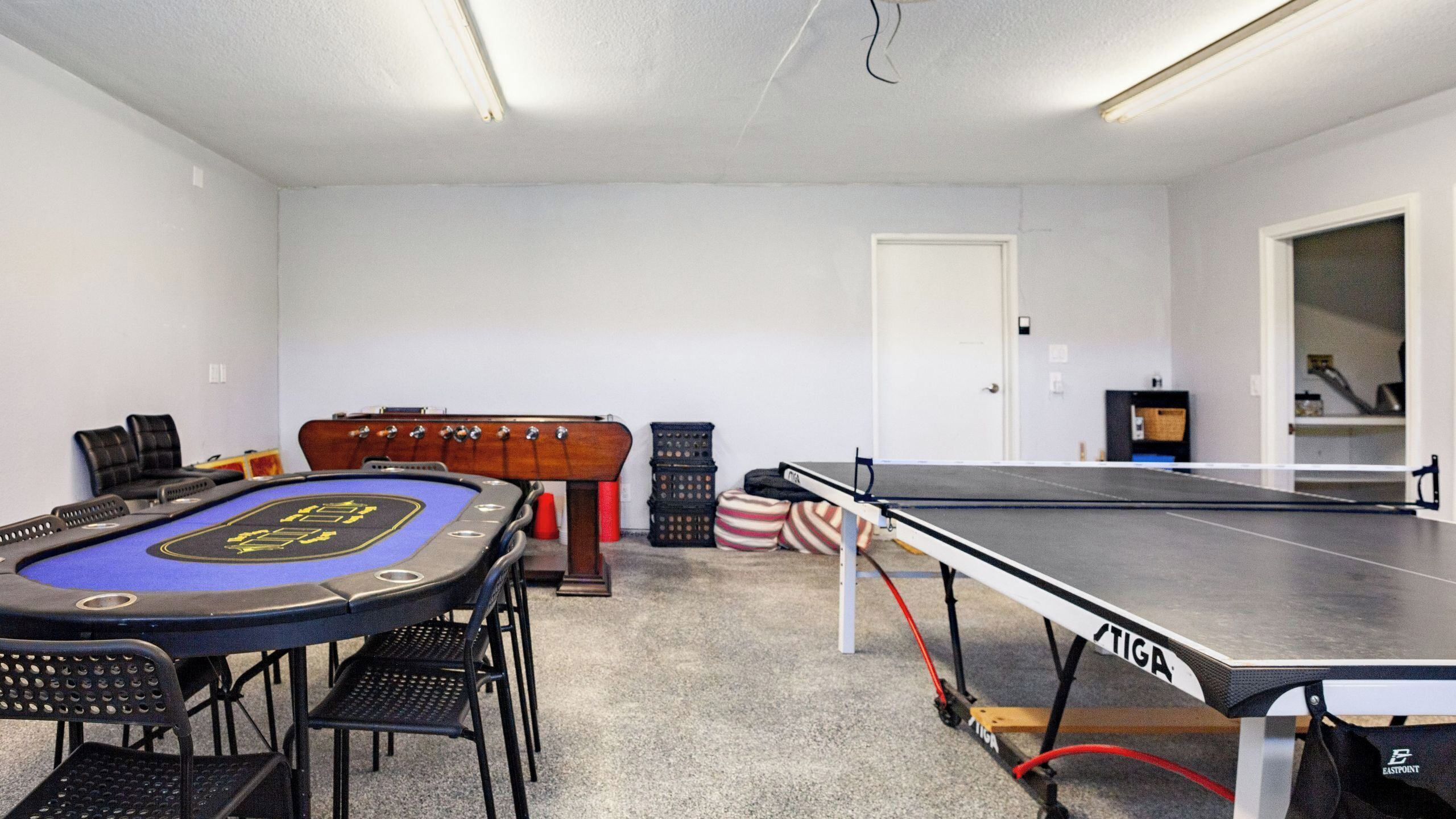 Een kamer met een pooltafel, stoelen, een pokertafel en een deur.