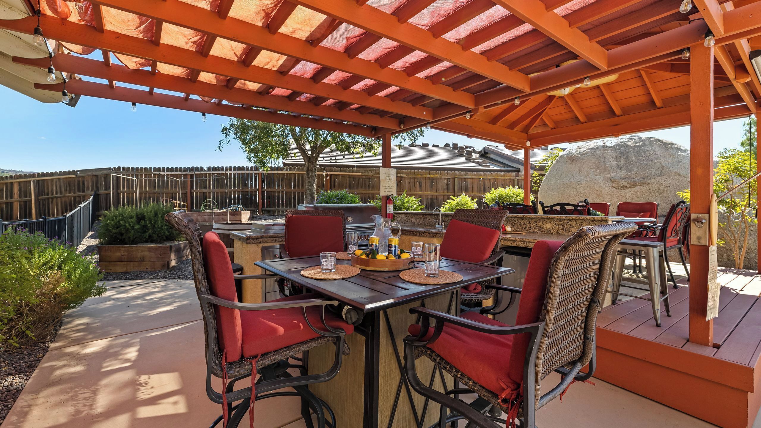 Un patio exterior con una pérgola de madera, una parrilla para barbacoa y una mesa lista para comer.