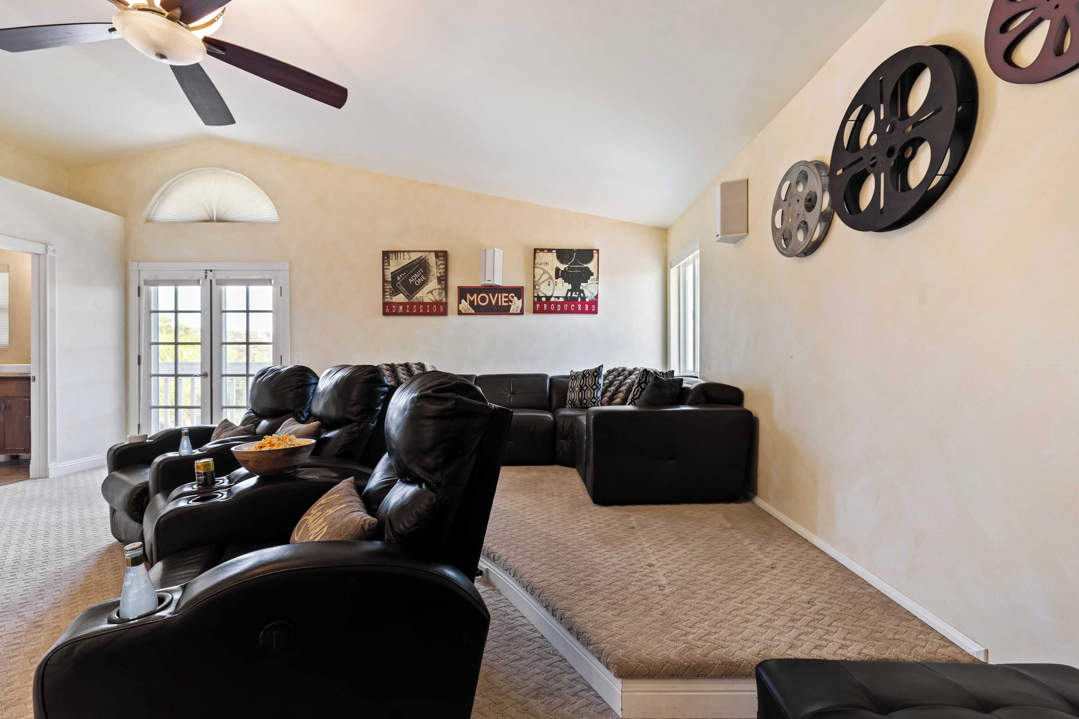 A spacious living room with a sectional sofa, a ceiling fan, and wall-mounted movie-themed decorations.