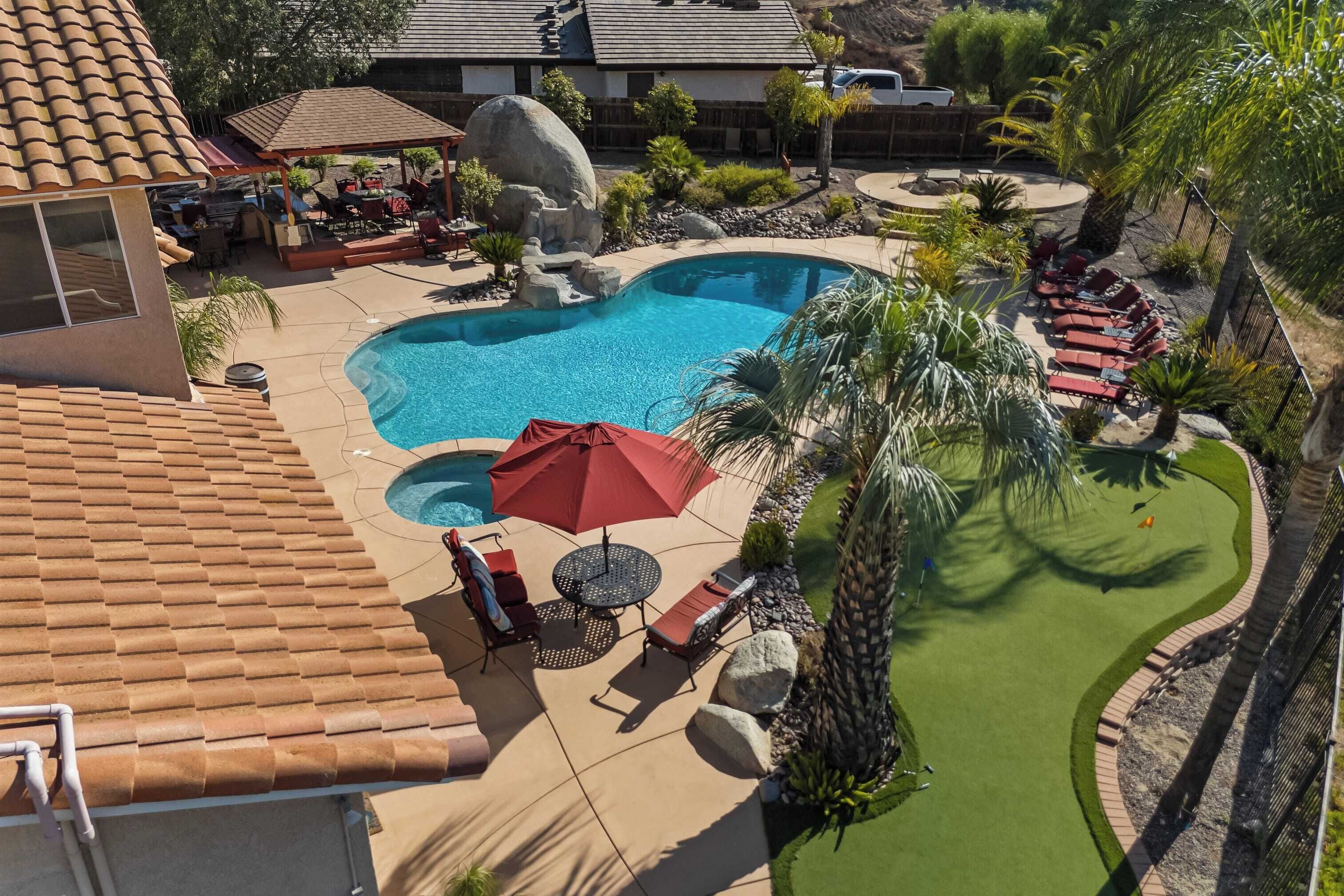 A backyard with a swimming pool, lounge chairs, and a patio area.