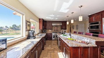 A spacious kitchen with a large island, built-in ovens, and a view of a swimming pool.