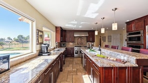 A spacious kitchen with a large island, built-in ovens, and a view of a swimming pool.