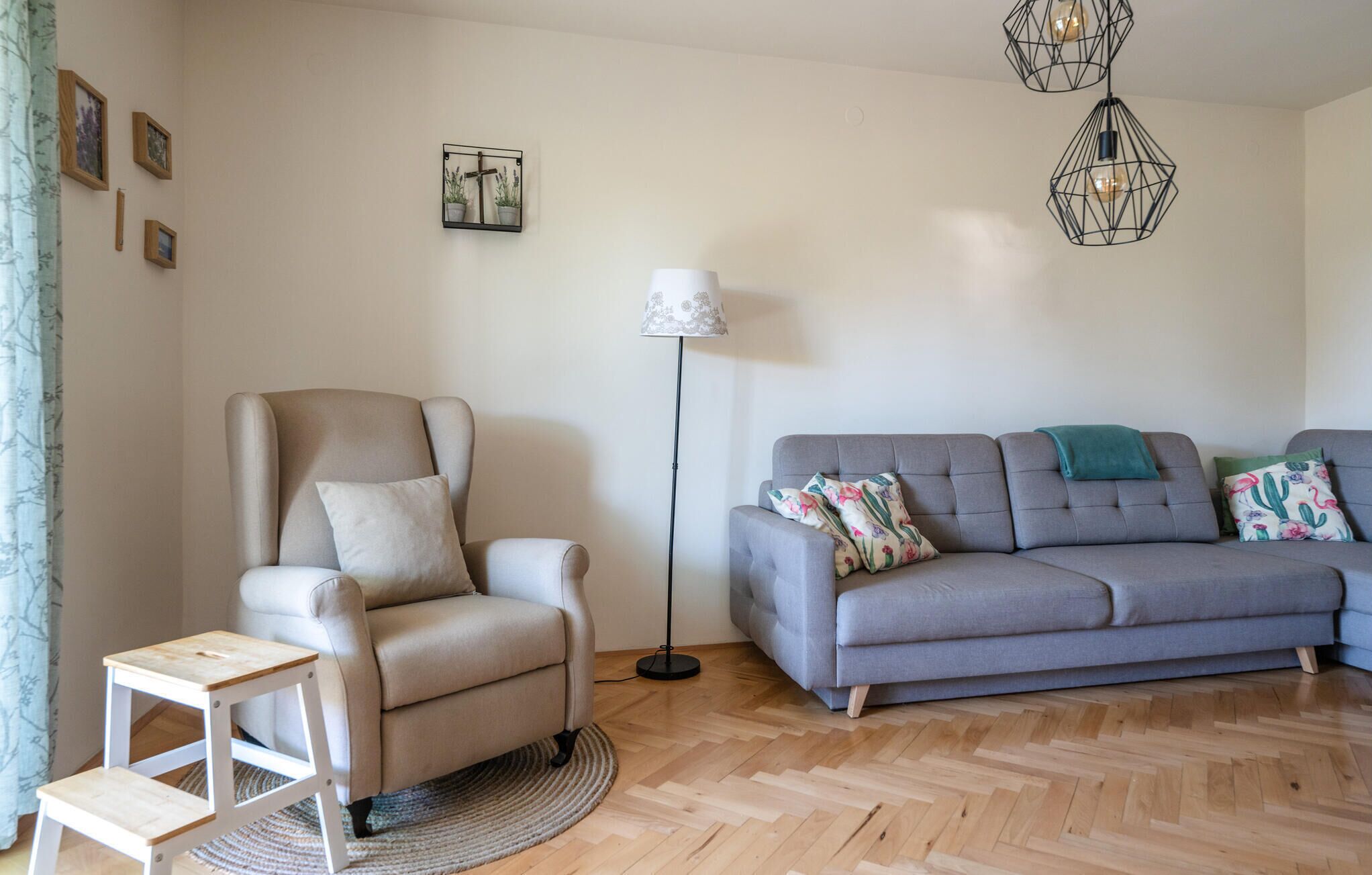 Un salon avec un canapé gris, un fauteuil beige, une petite table blanche et un lampadaire.