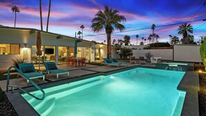 A modern outdoor pool area with lounge chairs, a dining area, and a well-lit building. - Modern Sunset: MCM color-filled classic (Palm Springs)