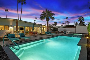 A modern outdoor pool area with lounge chairs, a dining area, and a well-lit building.
