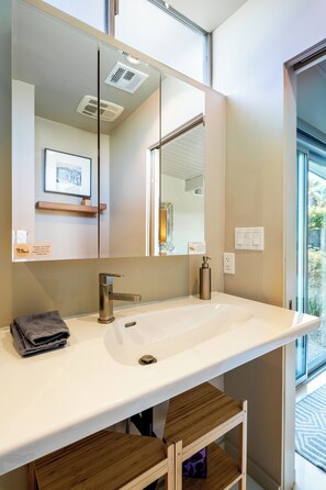 Une salle de bain moderne avec un grand miroir, un lavabo blanc et une étagère en bois.