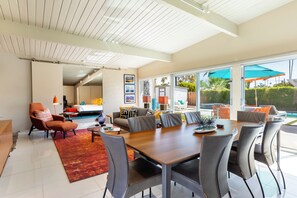 A spacious living area with a large dining table, comfortable seating, and a view of the outdoors. - Modern Sunset: MCM color-filled classic (Palm Springs)
