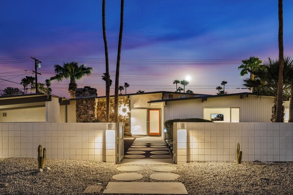 Une maison moderne avec une façade en pierre, une entrée bien éclairée et un chemin menant à la porte.