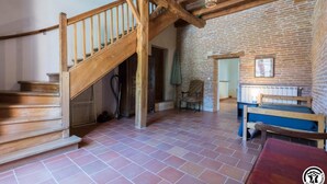 Una habitación rústica con una escalera de madera, un muro de ladrillo, una cama y una silla.