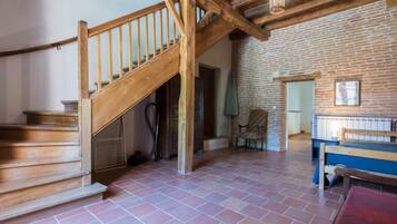 A rustic room with a wooden staircase, a brick wall, a bed, and a chair.