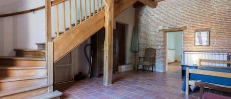 A rustic room with a wooden staircase, a brick wall, a bed, and a chair.
