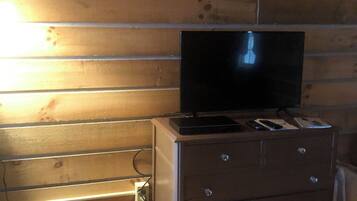Een houten blokhut van binnen, met een televisie op een dressoir, een mand met kleding en een stopcontact.