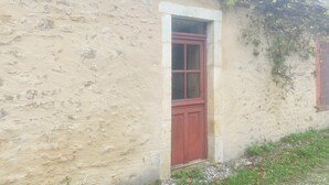 Un edificio rústico con una sola puerta roja y una ventana pequeña.