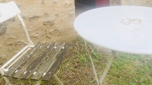 Un espacio de estar rústico al aire libre, con una mesa redonda, un banco de madera, una puerta roja y una pared de piedra con textura.