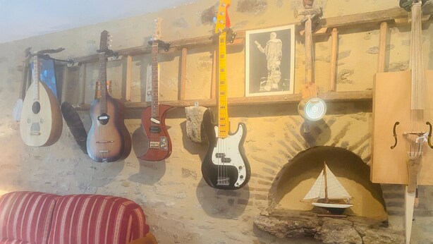 Una habitación con chimenea de piedra, un sofá a rayas rojas y varias guitarras colgadas en la pared.